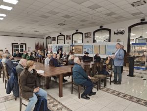 grupa ludzi siedzi na krzesłach przy stole słuchając wykładu