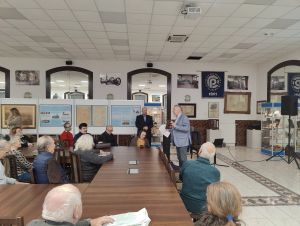 grupa ludzi siedzi na krzesłach przy stole słuchając wykładu