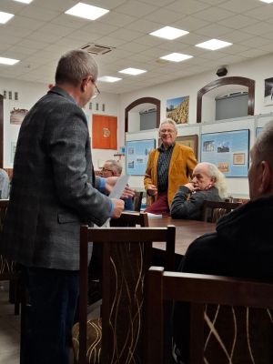 grupa ludzi siedzi na krzesłach przy stole słuchając wykładu