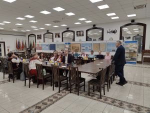 grupa ludzi siedzi na krzesłach przy stole słuchając wykładu