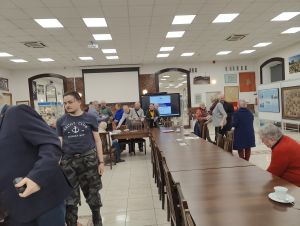 grupa ludzi siedzi na krzesłach przy stole słuchając wykładu